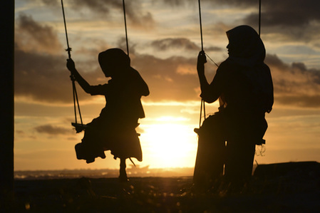 Silhouettes of a mother and child on a swing watching the sunset at Susoh beach.