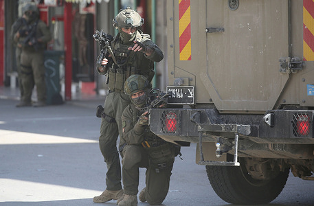 Israeli soldiers take cover next to Israeli military vehicles during a security operation in the Askar refugee camp. Israeli forces raided and searched Palestinian shops and arrested several young Palestinians during the operation which took place. Palestinian sources reported that a 20-year-old Palestinian man was killed and another wounded during clashes in the village of Beit Furik.
