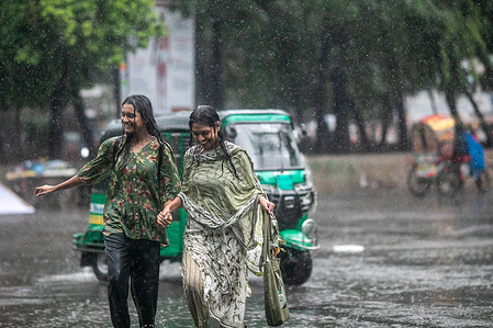 Women seen walking in the middle of the road on a rainy day. The heavy monsoon downpour made travel slow and dangerous.
