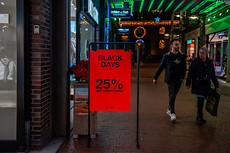 Two people are seen walking next to a poster announcing Black Friday deals from the store "Only & Sons". The only day of the week (Thursday) that stores open until 9 PM, they were already ready with Black Friday deals. About a third of Netherlands residents delay purchases to get a better deal on Black Friday. Black Friday is increasingly also becoming the time to switch internet and streaming services.