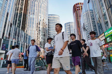 Young men in casual wear walk through Sanlitun's modern street with skyscrapers.