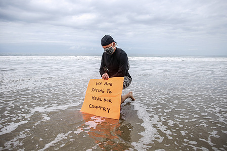 A protester holding a placard takes a knee in the water to pay respect to George Floyd during the demonstration.
Protesters marched from the Venice Beach Pier to the Santa Monica Pier to honour George Floyd and to call for reform to end police brutality.