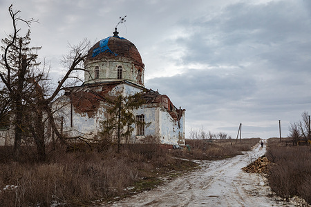 A heavily damaged church with a crumbling dome and peeling walls is seen in the Kharkiv region. Blue tarp covers sections of the roof near a muddy road. As a result of hostilities, more than 100 religious buildings of various denominations have been damaged or completely destroyed in the region, many of which hold the status of architectural monuments. The scale of the damage spans from modern churches in Kharkiv's residential neighborhoods to ancient cathedrals in Izium and Kupiansk hit by direct missile and aerial bomb strikes. Despite local communities' efforts to preserve the structures, a significant portion of these houses of worship remains in ruins, a fact documented by international missions as the systematic destruction of the region's cultural and spiritual heritage.