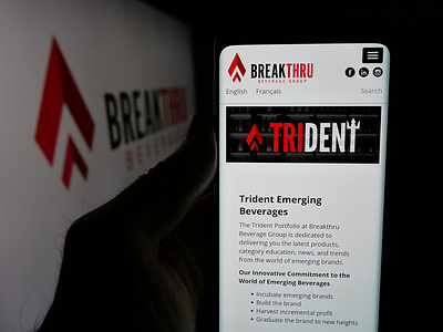 In this photo illustration, a person holding a smartphone with the website of US company Breakthru Beverage Group LLC on screen in front of logo.