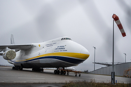 A Ukrainian Antonov An-124-100M cargo aircraft is seen at Leipzig/Halle Airport, with an airport windsock visible in the background.
