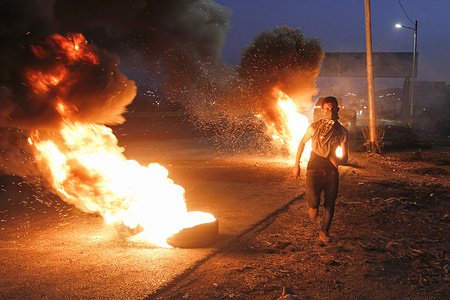 A Palestinian runs past burning tires during the demonstration at the Israeli Hawara checkpoint. 
Palestinians expressed their solidarity with the four prisoners who were arrested after escaping from the Israeli Gilboa prison near the Israeli Hawara checkpoint, south of Nablus in the West Bank. The lawyer said that the four prisoners live in difficult punitive conditions.