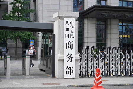 The stone pillar sign of the Ministry of Commerce of the People's Republic of China, the entrance gate, a security guard, a pedestrian, and part of the building's interior and exterior.