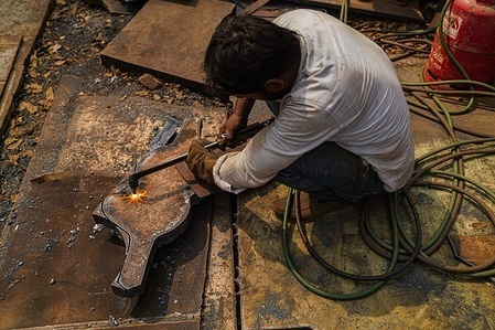 A laborer cuts a steel sheet at a workshop in Dhaka.