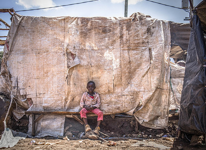 A young boy relaxing outside his small homemade house made with recycled Polypropylene sacks in Kibera slums.
In Africa’s largest and slowly developing Kibera Slums, well known for its highest growth in population and the densely connection and closeness of structures around the neighborhoods, not everyone is able to practice and take action recycling of waste products and plastic products. 
After the demolition of homes and businesses, located close by the railway line by the Kenya Railways, most residents are seen practicing the recycling of polypropylene sacks to build their new homes and little businesses stalls, as well as using them to plant vegetables such as Calles, Skuma Wiki, Beans, Onions, Tomatoes and more.
By recycling polypropylene sacks, these residents contribute in defending climate change by creating a reduction in the consumption of raw resources such as oil and propane gas. Due to its tough and rough texture, polypropylene bags are also used as in-house decoration of homes, carpets, shopping bags, and school bags.