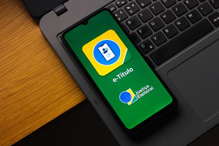 In this photo illustration, the e-Título (Brazil's digital voter ID) logo is displayed on a smartphone screen resting on a laptop.