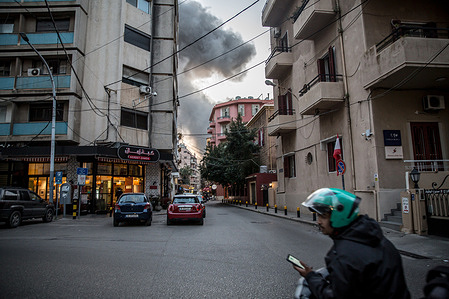 A Toters delivery driver rides past the smoke from an Israeli airstrike on Bachoura. Israel and Hezbollah returned to all-out war in March 2026.