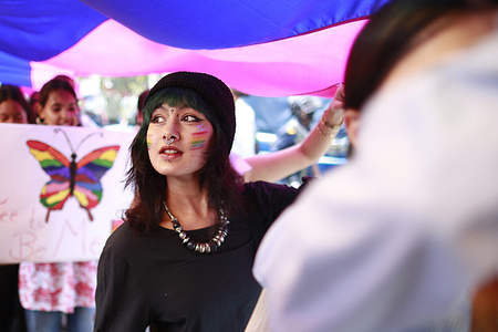 A woman holds a placard with a butterfly in rainbow colors during a Pride Parade celebrating the LGBTIQA+ community.