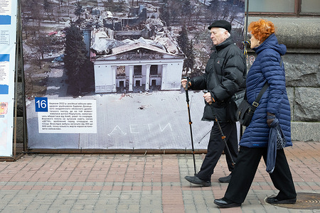 People walk near a picture of the destroyed Mariupol Drama Theater, destroyed by a Russian airstrike, in central Kyiv. The Drama Theater in Mariupol was destroyed on March 16, 2022, by a Russian Aerospace Forces airstrike. According to Ukrainian authorities, the theater served as a bomb shelter for approximately 600 civilians.