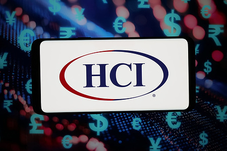 In this photo illustration, the logo of US financial company HCI Group Inc. is displayed on a smartphone in front of abstract background on computer screen.