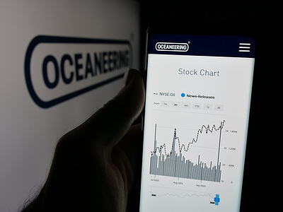 In this photo illustration, a person is holding a smartphone with the web page of Oceaneering International Services Inc. on screen in front of logo.