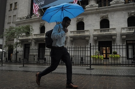 A person carries an umbrella and walks past the New York Stock Exchange in the Financial District in Manhattan, New York City during a rain shower.