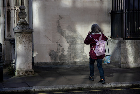 A visitor takes a photo from Banksy's mural in London. A few days after the newest Banksy's mural appeared on the wall of The Royal Courts of Justice in London it was partly washed off. Since then, tourists and locals visit the place to take photos of it.