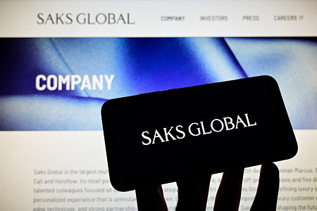In this photo illustration, the logo of American company Saks Global specializing in department stores and commercial real estate is seen displayed on a phone with the company's website in the background. Logo of the American company Saks Global on Wednesday, January 14, 2026, in Veranne, France. The company announced it was filing for bankruptcy.