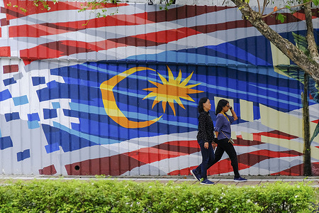 Women seen walk in front of a Malaysian flag mural at Kuala Lumpur. Daily life at Kuala Lumpur.