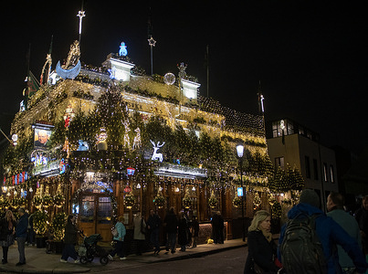 Tourists and costumers stand outside the Churchill Arms. The Churchill Arms is located near the Notting Hill Gate Station. It is the most Christmassy pub for over 30 years. This year nearly 100 conifer trees and 135000 fairy lights were used to decorate the pub outside.