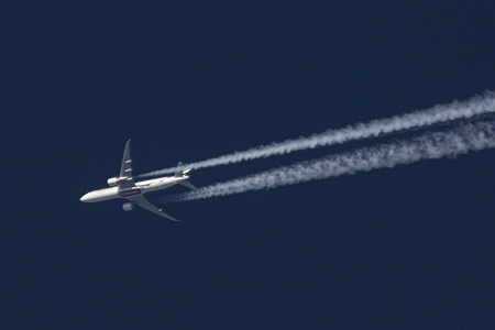 An Emirates Boeing 777 wide body aircraft is seen flying at 40.000 feet in the blue sky over the Netherlands. 
The overflying airplane creates contrails, the white condensation vapour lines. The plane is flying from Dubai DXB UAE to England, UK.