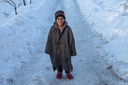 A Kashmiri kid poses for a picture while walking through a snow-covered street on a cold day after heavy snowfall in Budgam.