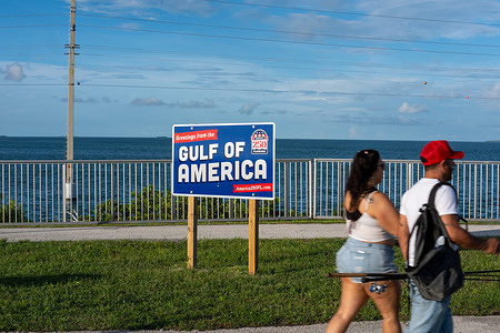 People walk past a "Gulf of America" sign that is posted overlooking the Gulf of Mexico in the Florida Keys.