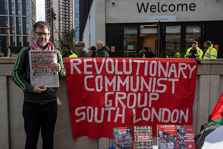 A protester stands with newspapers by a Revolutionary Communist Party's banner outside the UK Government HUB offices during the demonstration. Protesters gathered on the Ruskin Square by the new UK Government HUB offices in Croydon, London. Demonstrators intend to oppose the government immigration policies and to show their solidarity with refugees and migrants.