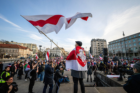 Wearing a small Belarusian flag around his shoulders, a man waves a much larger flag. On the afternoon of Sunday, the 29th of March, Belarusians in Warsaw gathered to celebrate Belarus Freedom Day with a march from Three Crosses Square to Castle Square in the old town. The participants marched with flags, banners, and a long Belarusian flag carried by those in attendance. Opposition leader Sviatlana Tsikhanouskaya and the Deputy Head of the United Transitional Cabinet of Belarus, Pavel Latushko, led the procession.