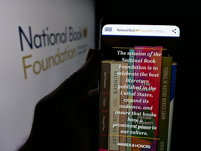 In this photo illustration, a person is holding a cellphone with the webpage of US organisation National Book Foundation on screen in front of logo.