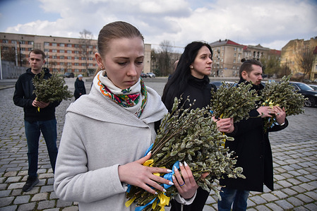 People hold bundles of willow branches near the graves of Ukrainian soldiers who died during the Russian-Ukrainian war at the Lychakiv cemetery in Lviv.