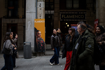 A group of people walk past a sign for a flamenco venue in the center of Madrid.