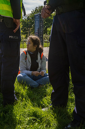 After being removed from the road, a climate activist sits behind the police detaining her. On May 6th, climate activists from the Last Generation (PL Ostatnie Pokolenie) group block the road leading to the Gdansk Bridge. The action is part of a series of events to coincide with High School exams and with the upcoming Polish presidential election. Rafal Trzaskowski, the incumbent Mayor of Warsaw is the Civic Coalition's presidential candidate. The climate activists direct their demands to him namely to redirect funding for new motorways to public transport and to introduce a public transport ticket for all priced 13.26 United States Dollar per month.
