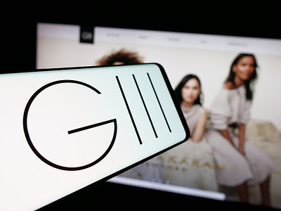 In this photo illustration, a smartphone with the logo of US clothing company G-III Apparel Group Ltd. is seen on screen in front of website.