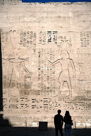 Foreign tourists admire reliefs and hieroglyphs inside Medinat Habu, the ancient Egyptian Mortuary Temple of Ramesses III on the West Bank of The Nile. Medinet Habu, a vast Egyptian archaeological site located on the West Bank of the Nile in Luxor, Egypt. It is most famous for the Mortuary Temple of Ramesses III, an architectural masterpiece renowned for its massive scale, outstanding preservation and intricately decorated wall reliefs detailing historic military victories and religious ceremonies.