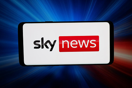 In this photo illustration, the logo of British television channel Sky News is displayed on a smartphone in front of abstract background on computer screen.
