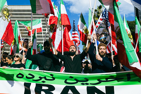 Demonstrators march through downtown Los Angeles during an Iran solidarity protest, holding pre-revolution Iranian flags bearing the lion and sun emblem and a Persian-language banner, as members of the Iranian diaspora rally near Los Angeles City Hall to oppose the current government in Iran.