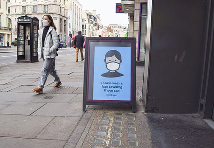 A woman wearing a face mask as a precaution against the spread of coronavirus walks past a sign outside a store in Central London encouraging people to continue to wear face masks if they can, as England ends mandatory face coverings in indoor public spaces.