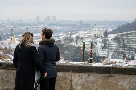 A couple observe general view of the snow-covered roofs in background in historical city center of Prague. First snowfall of the season is observed in Czech capital Prague.