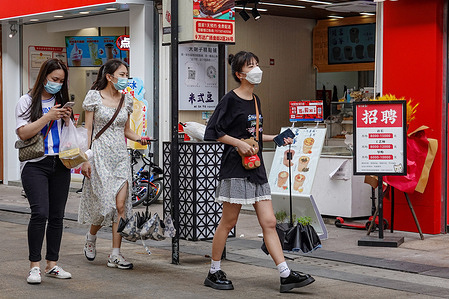 Three young women wearing face masks as a preventive measure against the spread of coronavirus walk on a pedestrian street.