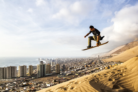 Sandboarder jumping a high dune with the city of Iquique in the background, in coastal Atacama Desert.
Sandboarding is an activity similar to snowboarding but takes place on sand dunes rather than snow-covered mountains. It involves riding across or down a dune while standing with both feet strapped to a board. It gain popularity during the recent 2 decades and the sport is especially popular in South America.