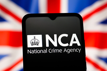 In this photo illustration, the NCA (National Crime Agency) logo is seen displayed on a smartphone screen with the UK flag in the background.