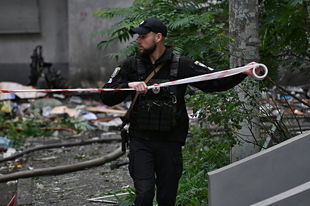 A police officer unrolls a cordon tape at the site where a Russian strike drone hit an apartment building during a Russian attack.