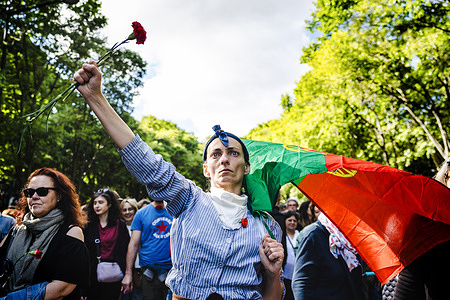 A woman holds a carnation and the flag of Portugal during the parade on the streets of Lisbon city center to celebrate the 50th anniversary of the Carnation Revolution. April 25, 2024 marks the 50th anniversary of a revolution led by the military and supported by the Portuguese people to overthrow the dictatorial regime of the Estado Novo, which became known as the Carnation Revolution. On April 25, 1974, democracy was restored and since then this 'Freedom Day' has been marked as a national holiday in Portugal.