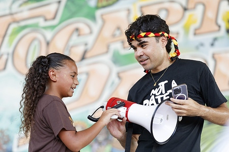 A girl prepares to speak to the crowd through a megaphone during the Invasion Day rally. Members of the local Aboriginal community and allies gathered in Cairns' Fogarty Park to mark Invasion Day, with the celebration of the 26th January Australia Day public holiday being marked as a date synonymous with Aboriginal and Torres Strait Islander people suffering and persecution since British colonial rule. Speakers told the crowd of ongoing unjust practices and poor outcomes involving health for Aboriginal people, land rights and police. Organiser Manny Williams described the demonstration as a peaceful, truth-telling event.