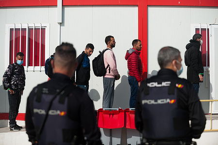 Two police officers stand guard as Migrants wearing face masks are waiting to be assisted by Spanish Red Cross after their arrival at Malaga Port.
An intensive border patrol by Moroccan’s authorities has caused a drastic drop in the number of migrants that try to reach the Spanish coasts across Alboran Sea route, the arrival of migrants toward Canary Islands coasts (one of the most dangerous migration routes) has increased during the last months.