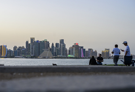 People gather on the Doha Corniche on a hot summer evening, looking toward the West Bay skyline in Doha.