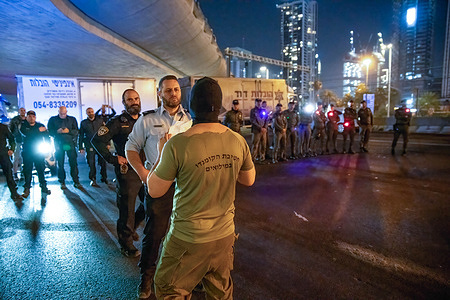 Israeli police officers faces a masked protester wearing a T-shirt of the reserve Commando brigade while holding a sign during the demonstration. Over 200,000 people protested in Tel Aviv against Netanyahu’s far-right government and its controversial legal reform.