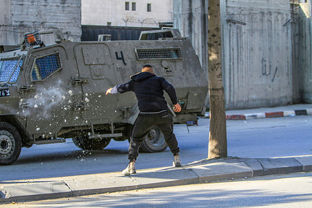 A Palestinian youth throws stones at the Israeli army vehicle during an army raid on the house of the Palestinian gunman, Ahmed Al-Kharraz, to arrest him in the city of Nablus in the occupied West Bank.