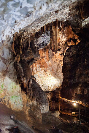 Interior view of the Su Mannau Cave (Grotte di Su Mannau), a massive karst cave system located in Fluminimaggiore, Sulcis-Iglesiente region, southwestern Sardinia. The cave features striking limestone formations, with stalactites and stalagmites reflected in the crystal-clear turquoise waters of an underground lake. Illuminated for guided tours, the cave is also an archaeological site that once served as an underground temple for water worship during the Nuragic, Punic, and Roman periods.